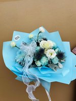 Ocean Serenade bouquet featuring white roses, white lisianthus, light blue chrysanthemums and blue thistle wrapped in blue paper with white ribbon...