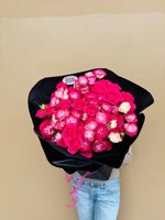Large bouquet of pink and white roses mixed with ranunculus wrapped in black paper, held by person wearing jeans