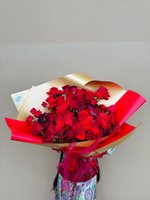 Bouquet of red roses and orchids wrapped in gold and red paper with a red ribbon