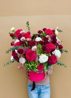 Person holding a luxury pink hatbox filled with burgundy and pink roses, burgundy dahlias, white carnations, and baby's breath with eucalyptus foli...