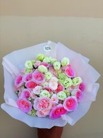 Pastel pink and green flower bouquet with roses, lisianthus, and carnations wrapped in white paper.