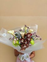 Elegant hand-tied bouquet featuring burgundy spotted orchids, cream calla lilies, and purple statice wrapped in white tissue paper