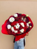 Person holding Christine bouquet with red and white carnations wrapped in burgundy paper against beige background