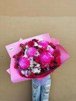 Jessica bouquet with bright pink chrysanthemums, white chrysanthemums, and dark red burgundy gerberas wrapped in pink paper, held against a beige b...