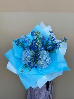 Hand-tied blue bouquet with light blue hydrangeas, blue delphiniums, and white baby's breath wrapped in blue and white tissue paper