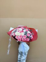Hand-tied bouquet of pink and white roses with dusty miller foliage, wrapped in burgundy paper with white ribbon, held against a neutral background