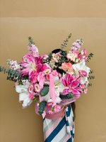 A large hatbox arrangement of pink lilies, roses, and carnations with greenery.