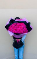 Person holding large bouquet of 25 bright magenta roses wrapped in black and purple paper against neutral background