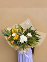 A bouquet of sunflowers, white chrysanthemums, and peach carnations with greenery, wrapped in warm-toned paper.