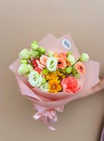 Coral Dawn bouquet featuring coral gerberas, yellow chrysanthemums, white lisianthus, coral carnations and green ranunculus wrapped in soft pink pa...