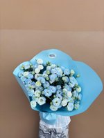 Hand-tied bouquet of white and light blue lisianthus flowers wrapped in blue paper, held against a neutral background