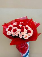Bouquet of crimson red and blush pink roses wrapped in bold red paper with golden trim.
