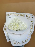 Three white hydrangea flowers wrapped in white paper with gold 'EVERYDAY I LOVE YOU' text, held against a beige background