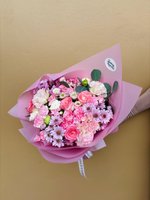 Bouquet of pink roses, carnations, lilac chrysanthemums, and white flowers wrapped in soft pink paper.