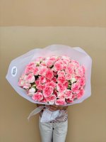 Large bouquet of 19 pink and white spray roses wrapped in white tissue paper with ribbon, held by person against neutral background