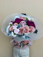 Person holding Rogue bouquet with pink roses, white spray roses, purple carnations and dusty miller foliage wrapped in white paper