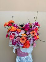 Bright orange and pink flower arrangement with roses, gerberas, and carnations in a pink hat box.