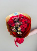 Hand holding Ruby bouquet with deep red roses and white chrysanthemums with burgundy edges, wrapped in gold and red paper with red ribbon