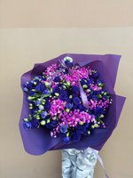Royal Mystique bouquet featuring deep blue roses and bright pink baby's breath wrapped in purple paper against a neutral background