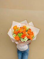 Person holding Vivian bouquet with orange roses, green chrysanthemums, and white baby's breath wrapped in white and gold paper