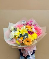 Colorful hand-tied flower bouquet with yellow chrysanthemums, pink and orange gerberas, white lisianthus, orange roses, and pink alstroemeria wrapp...