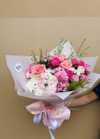 A bouquet of pink roses, lisianthus, carnations, and chrysanthemums with lush greenery, wrapped in white.