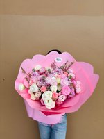 Princess bouquet held by person in jeans, featuring pink and white roses, lisianthus, and ranunculus wrapped in pink paper against beige wall