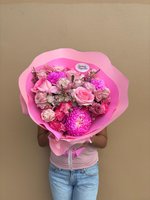 Person holding a large pink wrapped bouquet with pink roses, magenta chrysanthemums, spray roses and white wax flowers against a beige background