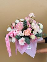 A pastel pink bouquet featuring carnations, peach roses, white lisianthus, and chrysanthemums wrapped in pink paper.