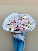 Person holding large romantic bouquet wrapped in white paper with pink and white roses, baby's breath, and green chrysanthemums tied with white rib...