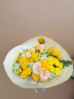 Sunny bouquet featuring yellow roses, white and pale pink lisianthus, yellow chrysanthemums, and baby's breath wrapped in cream paper