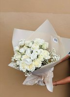 A classic white bouquet featuring roses, lisianthus, and baby’s breath wrapped in soft neutral paper.