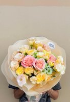 Bouquet with pink roses, white lilies, and yellow orchids in soft wrapping.