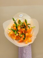 Golden Flame bouquet featuring eight vibrant orange lilies with green foliage, elegantly wrapped in cream paper and held against a neutral backgrou...